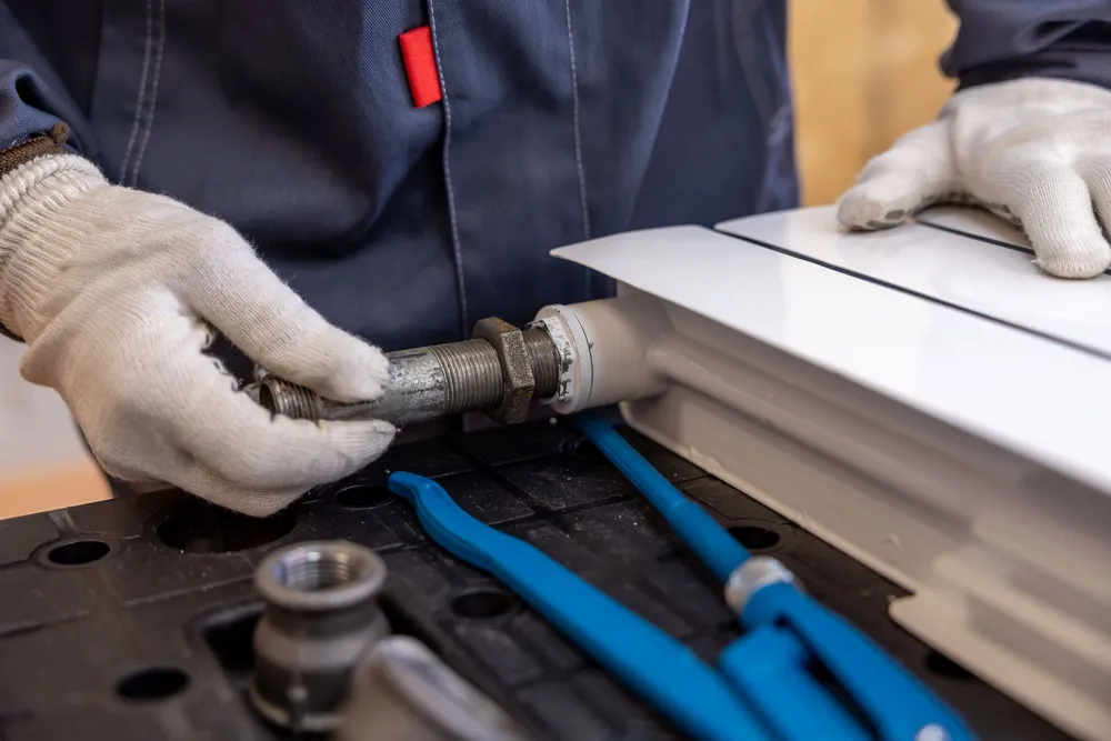 Plumber's gloved hands using tools to work on a threaded pipe fitting during a repair