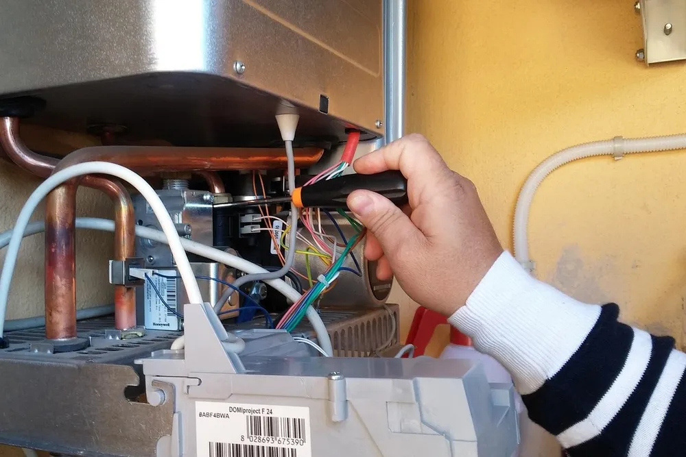 Technician repairing an open residential water heater unit, checking internal wiring and components